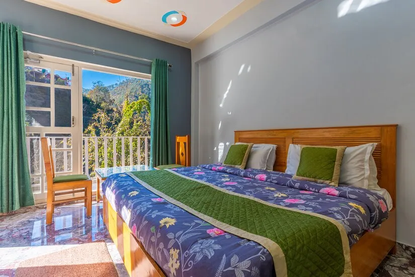 Deluxe Hill View room with green curtains and open balcony doors looking across the wooded hillside