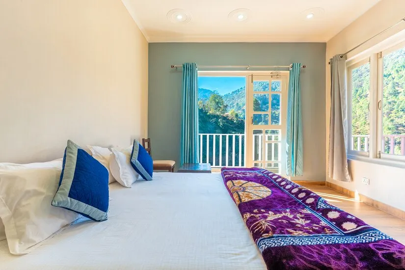 Deluxe Room with a wide bed, blue cushions and balcony doors opening onto the hillside