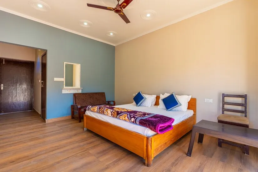 Standard Room with a wooden double bed, teal accent wall, wooden flooring and a bench under the window